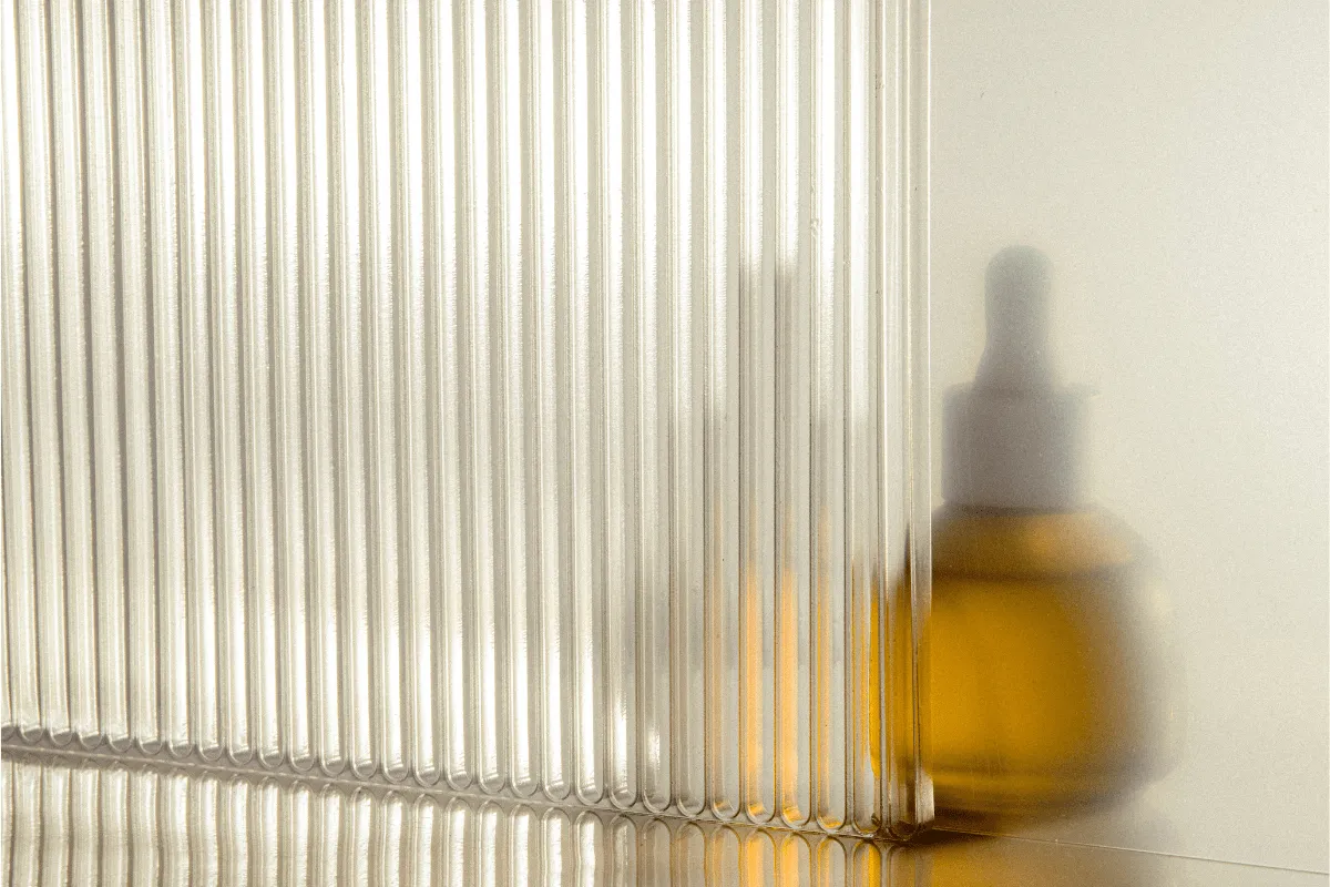 Amber glass dropper bottle obscured behind ribbed translucent panel.