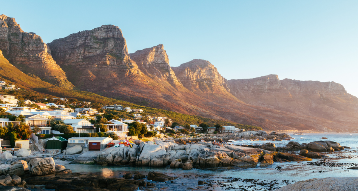 Coastal homes in Bakoven, Cape Town, set against the Twelve Apostles mountain range at golden hour.