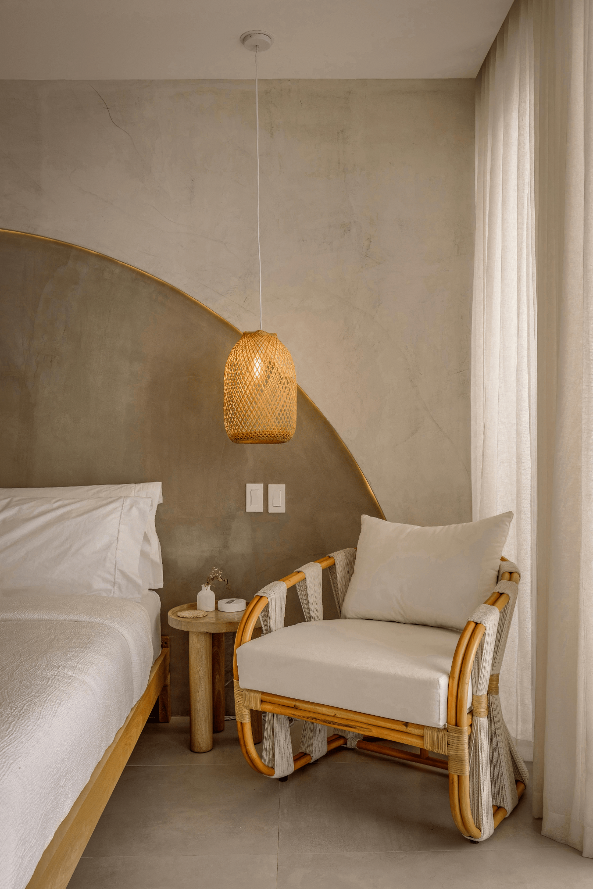 Calming bedroom with curved plaster wall, organic bedding, and rattan lounge chair.