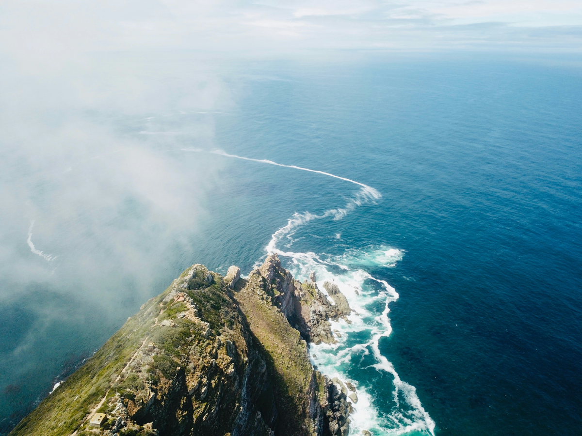Aerial view of Cape Point’s rugged peninsula with waves crashing against the steep cliffs under a misty sky.