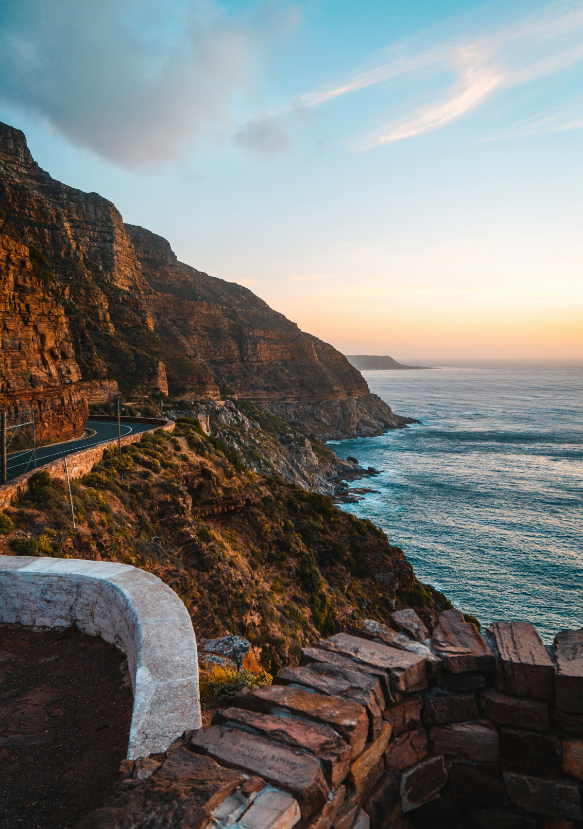 Winding Chapman’s Peak Drive hugging the cliffs at golden hour, overlooking the Atlantic Ocean in Cape Town, South Africa.
