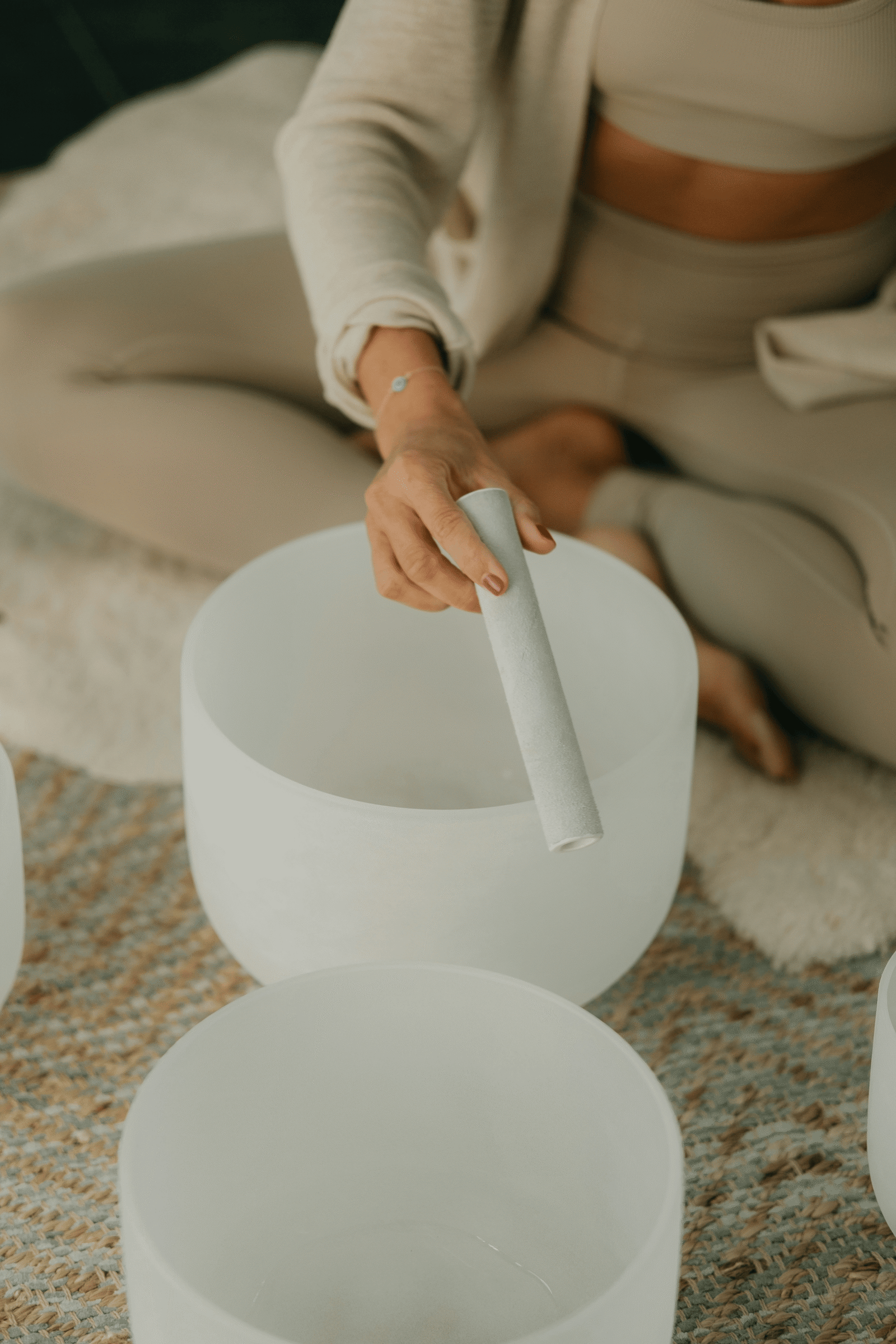 Close-up of hand using a mallet to activate crystal singing bowls on textured rug.