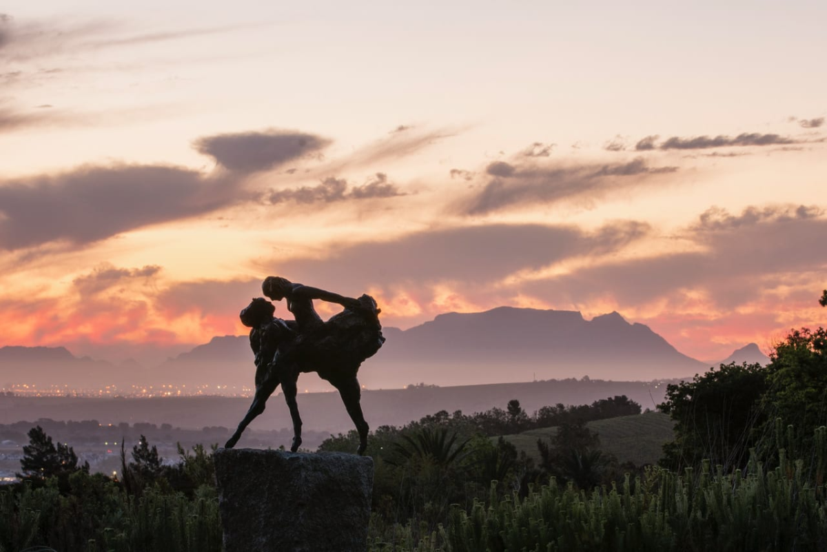 Silhouette of a bronze sculpture at Dylan Lewis Sculpture Garden set against a vivid sunset sky with mountains in the background near Cape Town, South Africa.