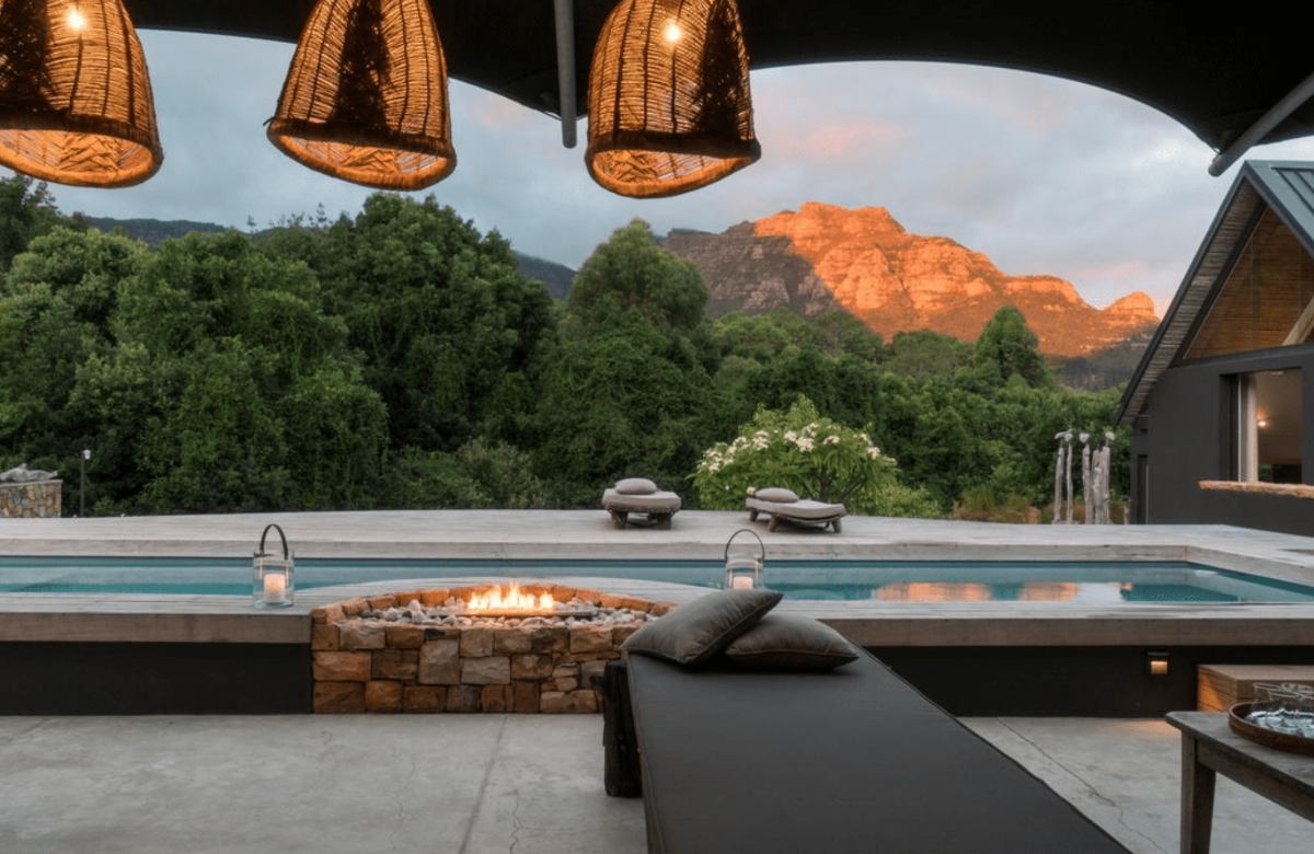 Tranquil poolside scene at Future Found Sanctuary in Cape Town with a fire pit, loungers, and mountain views at golden hour.