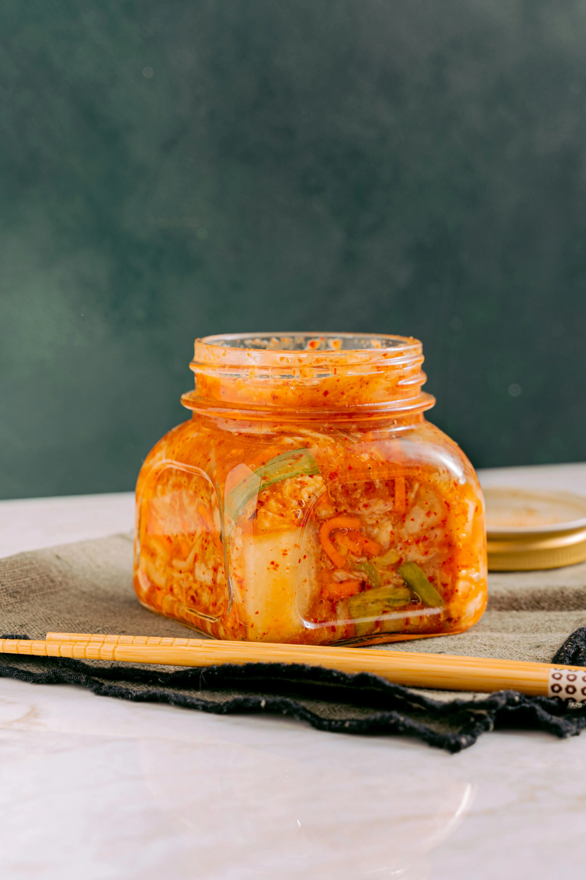 A square glass jar filled with vibrant, spicy Korean kimchi.