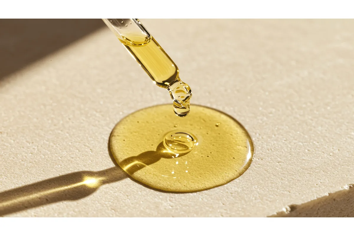 Close-up of golden facial oil dropped from a pipette onto a neutral surface.