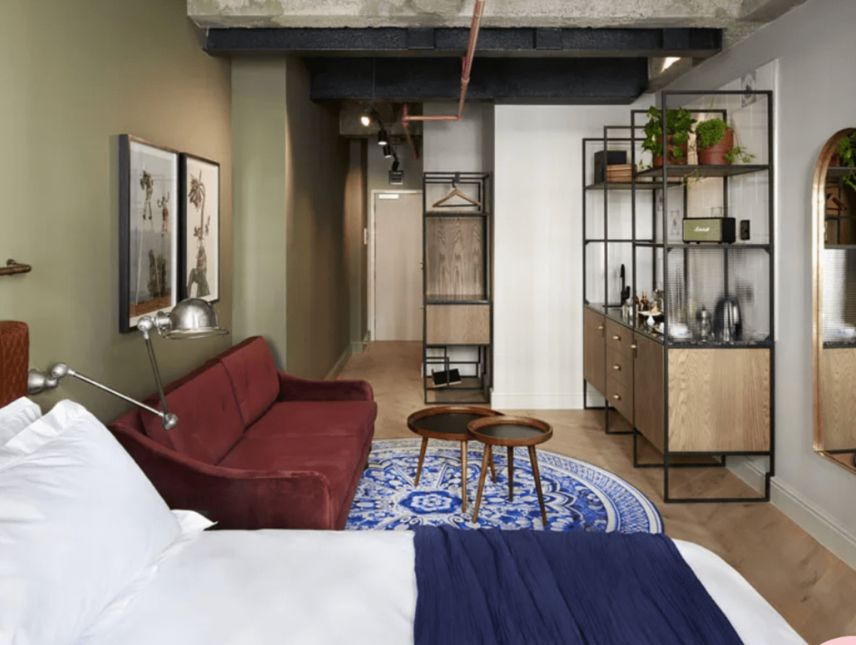 Stylish Cape Town hotel room at Gorgeous George with industrial shelving, velvet sofa, circular blue rug, and open-plan kitchenette.