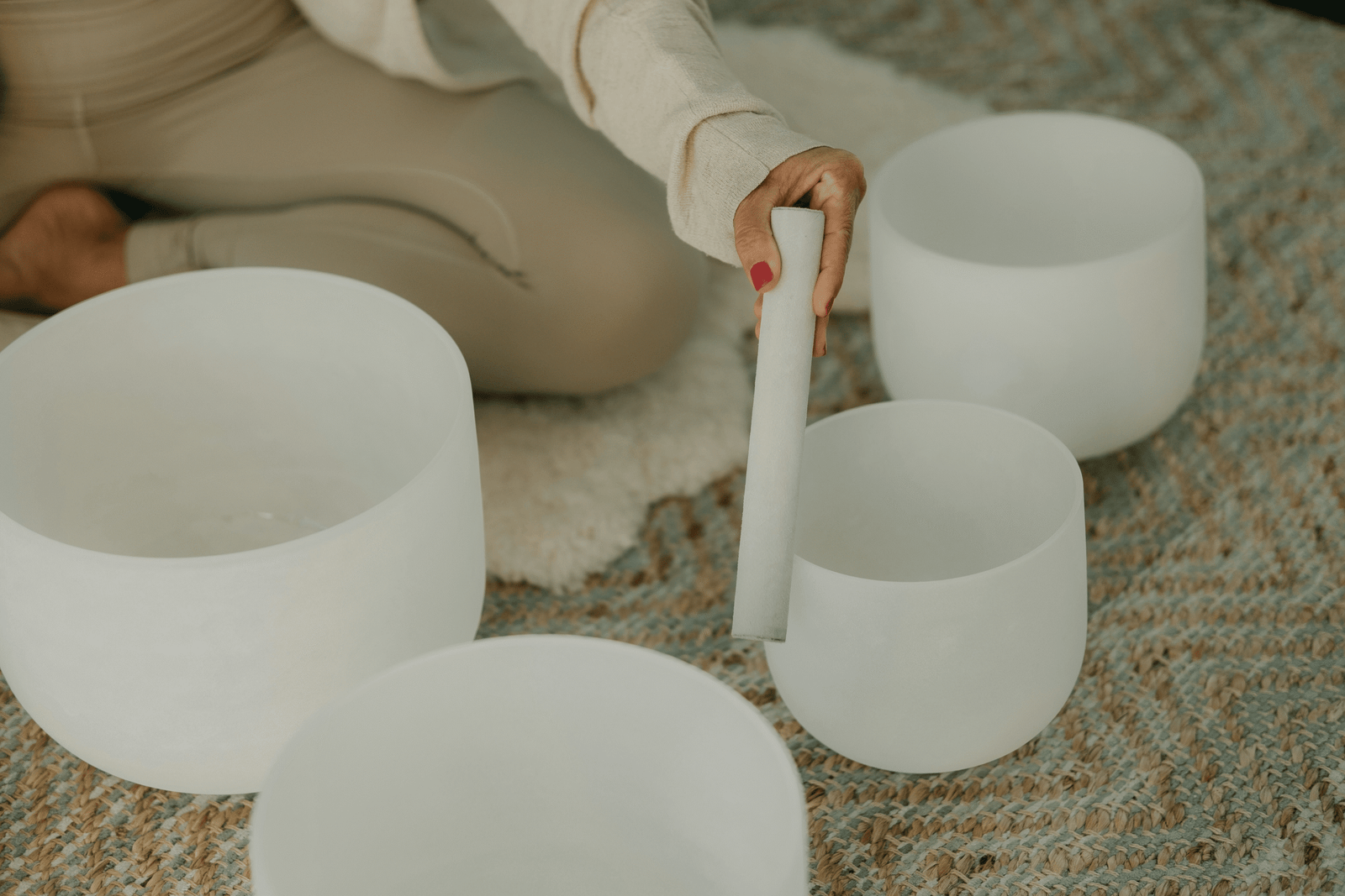 Hand gently playing white crystal sound bowls on a woven mat for sound healing.