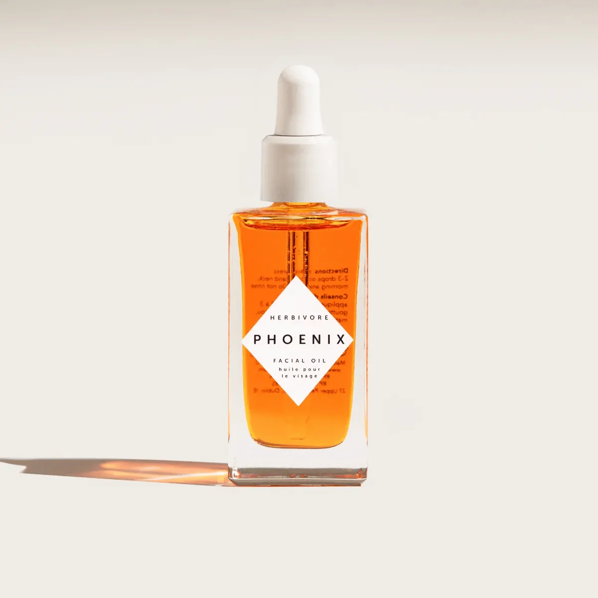 Herbivore Phoenix facial oil bottle with vibrant orange hue on neutral background.