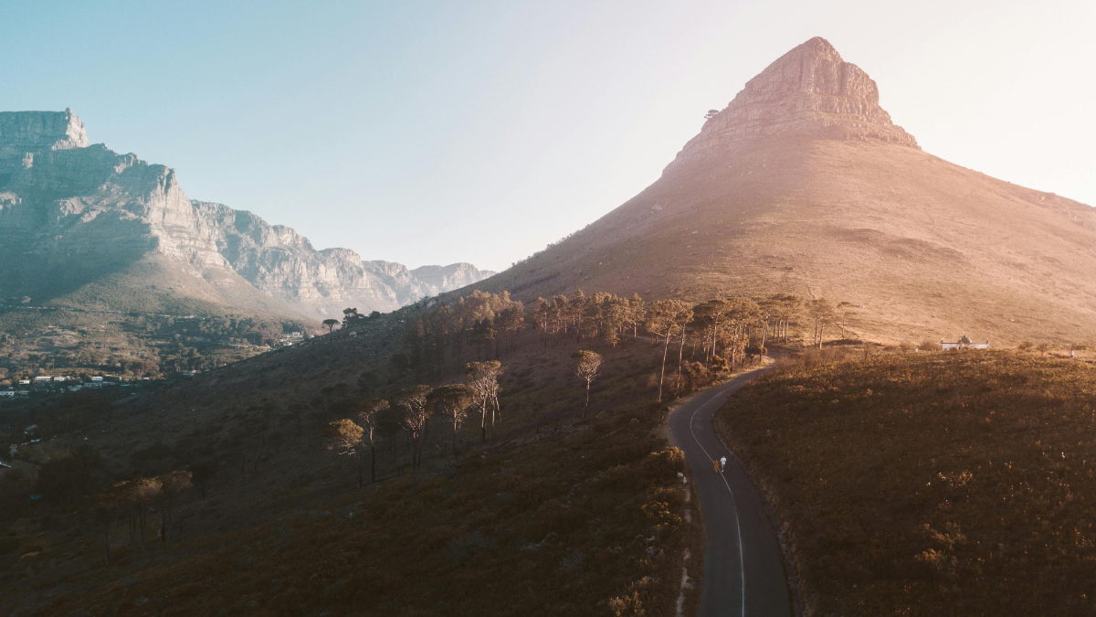 Winding mountain road leading to Lion’s Head with Table Mountain in the background.
