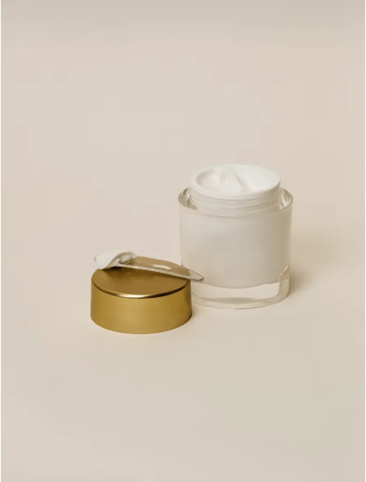 Minimalist glass jar of white face cream with a gold lid.