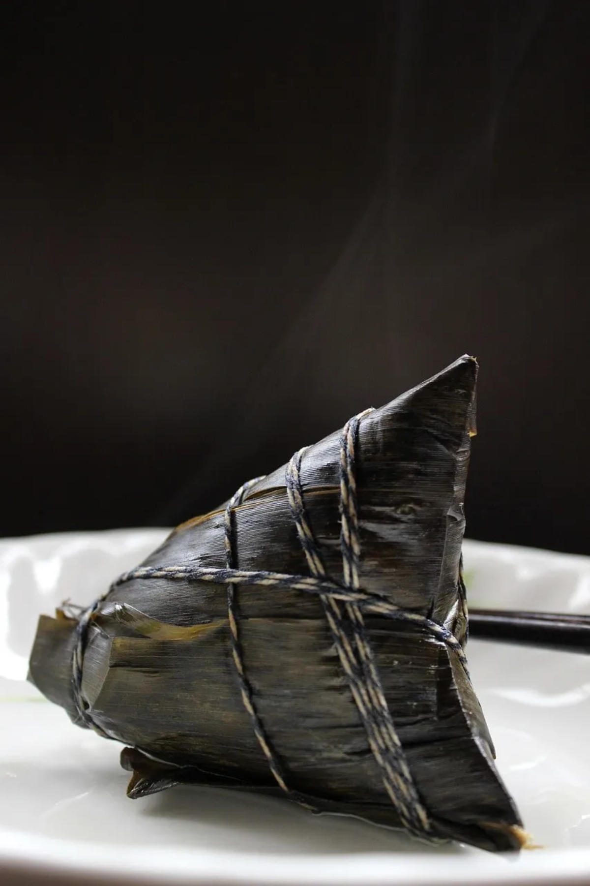 Close-up of a traditional Mexican tamale wrapped in dark bamboo leaves.