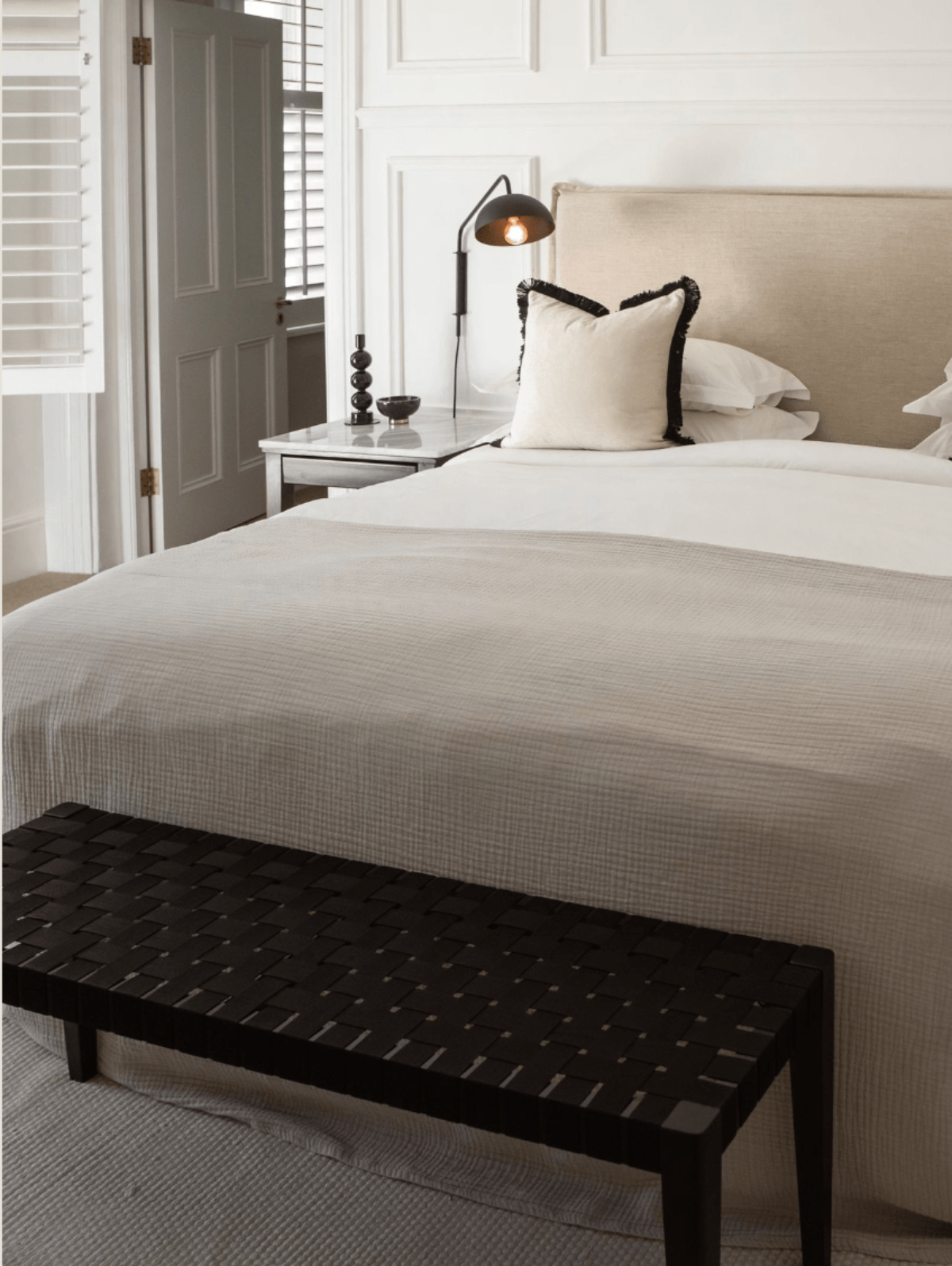 Serene boutique hotel room at NOAH in Cape Town featuring a neutral-toned bed, marble side table, black woven bench, and clean white wall paneling.