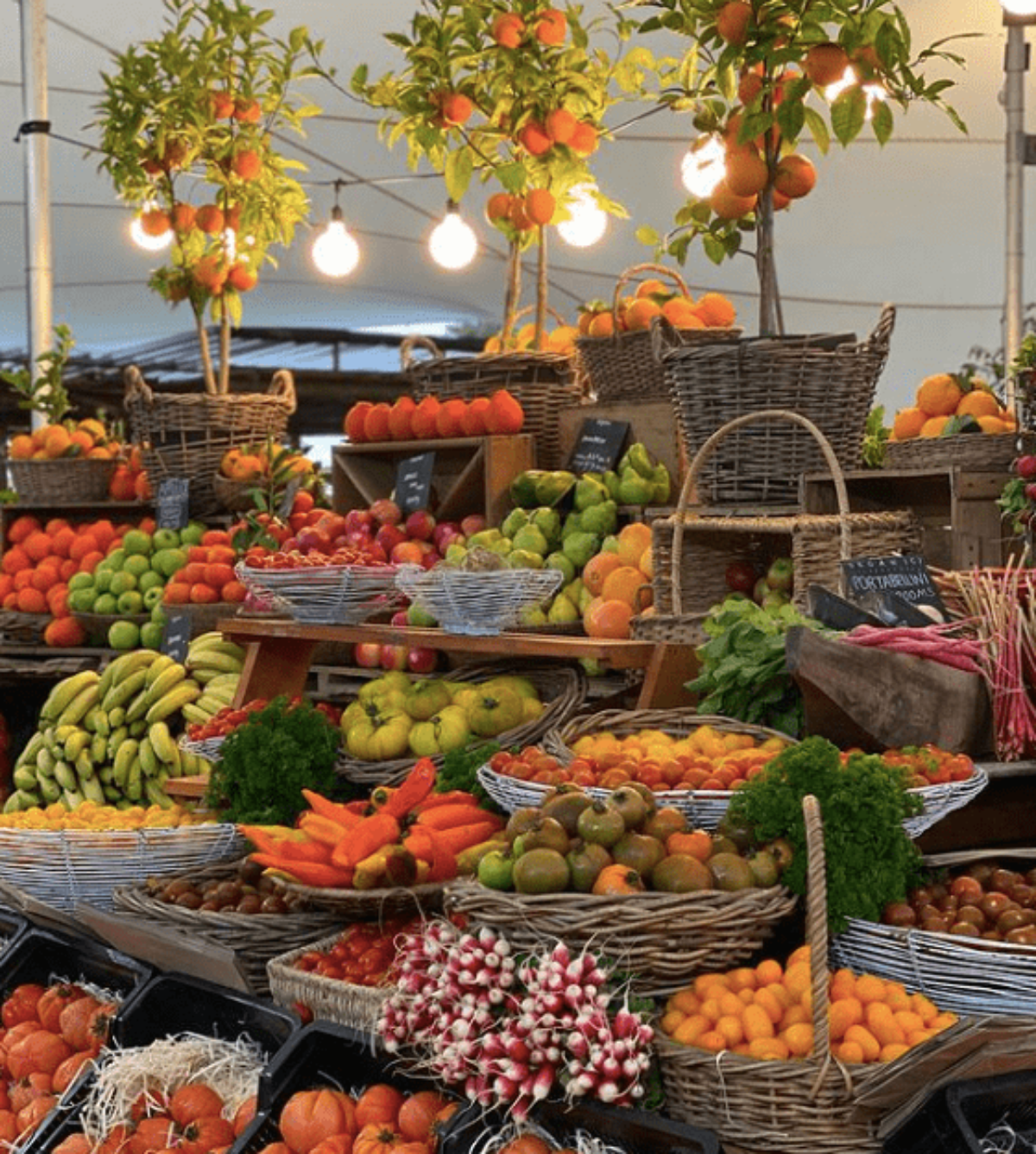 Abundant display of fresh produce at Oranjezicht City Farm Market in Cape Town, featuring baskets of vibrant fruits and vegetables under warm market lighting.