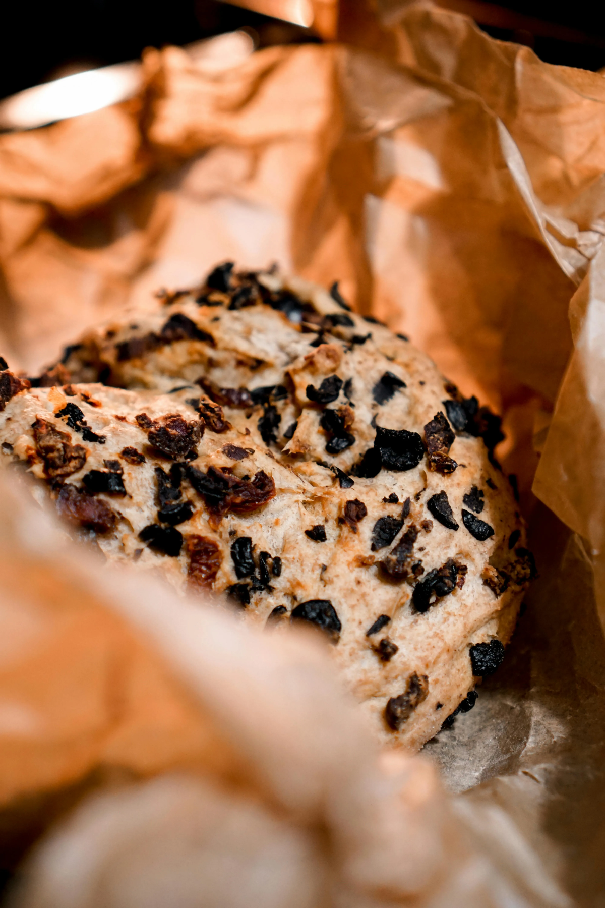 Close-up of an olive-studded Portuguese artisan loaf nestled in crinkled baking paper.