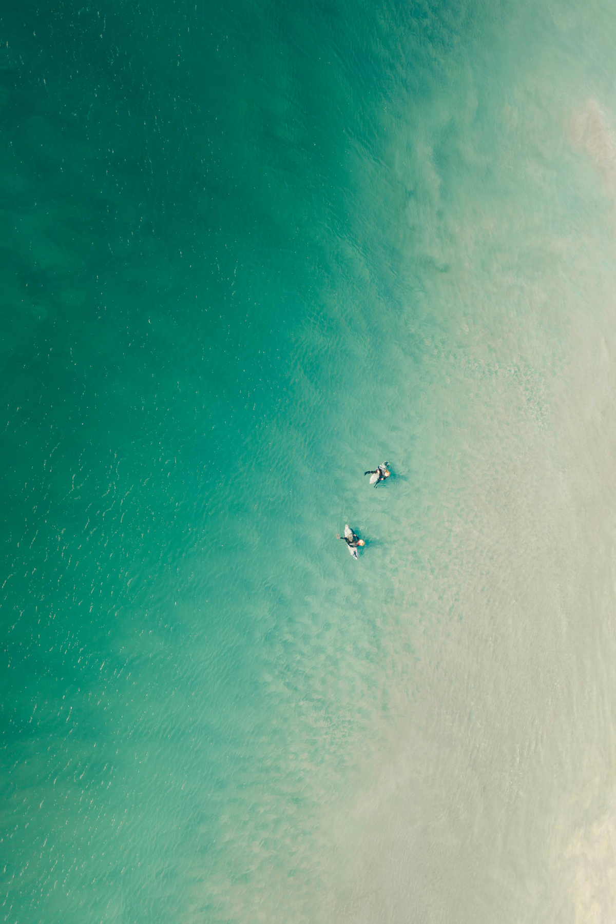 Aerial view of two surfers floating in clear turquoise water