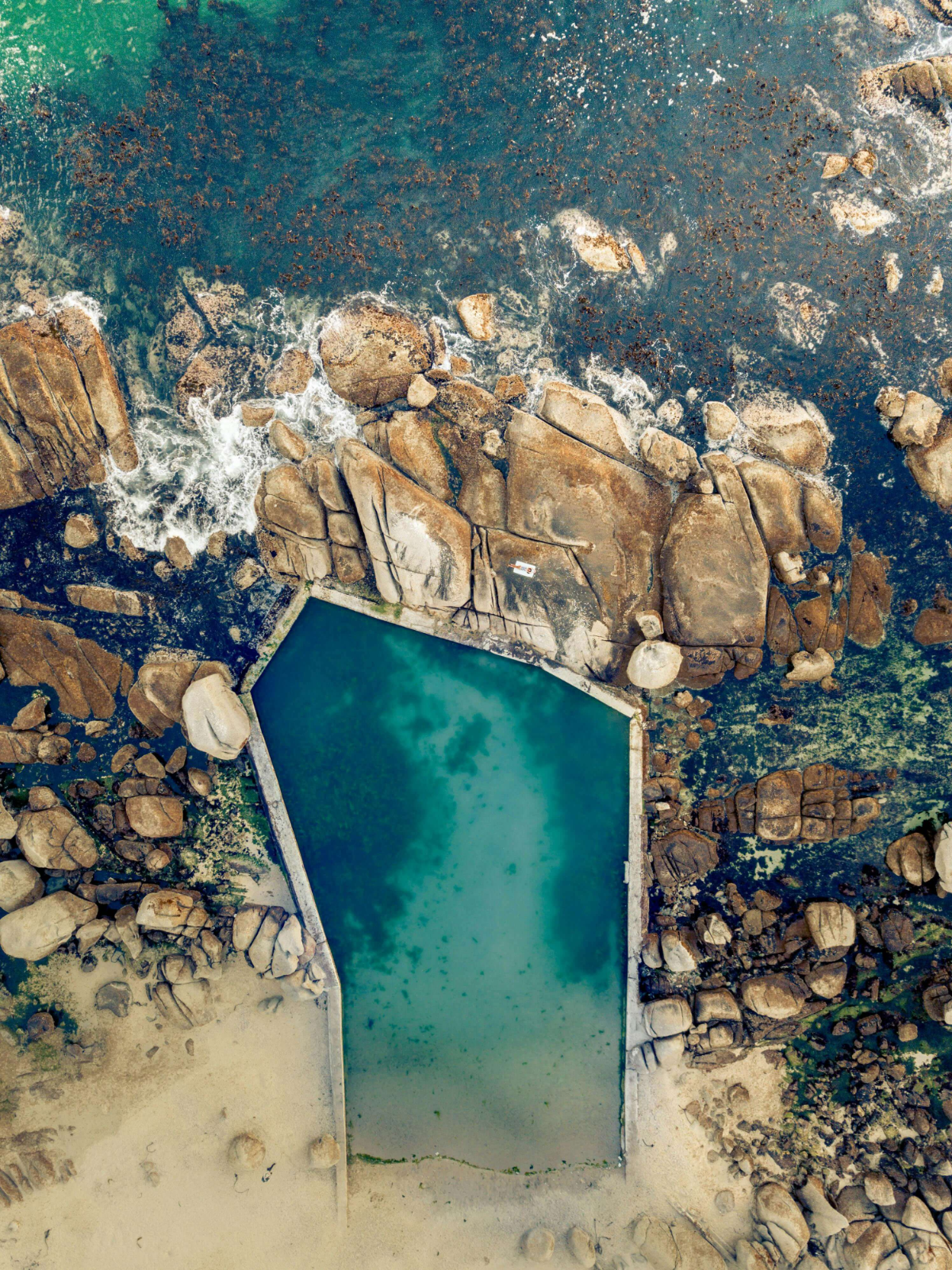 Aerial shot of natural ocean pool surrounded by rugged coastline and turquoise sea.