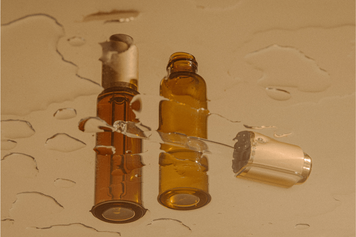 Amber apothecary-style oil bottles with dropper caps reflected on a wet surface, styled with warm lighting.