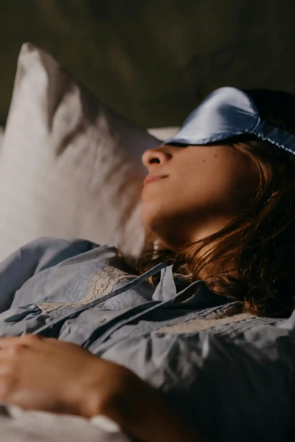 Woman resting on a white pillow while wearing a light-blue silk sleep mask for a peaceful night’s sleep.