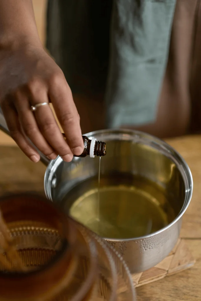 Brown glass bottle pouring essential oil into melted wax during handmade candle-making process.