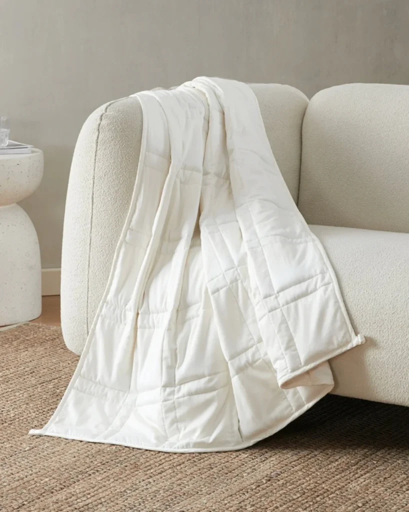 Baloo weighted blanket in cream draped over a textured sofa in a calm, neutral living space