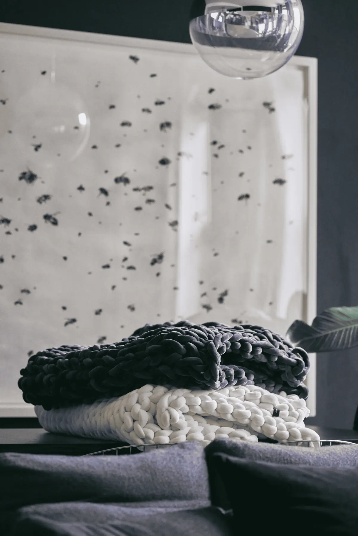 Folded Bearaby chunky-knit weighted blankets styled on table in modern living room beneath glass pendant light.
