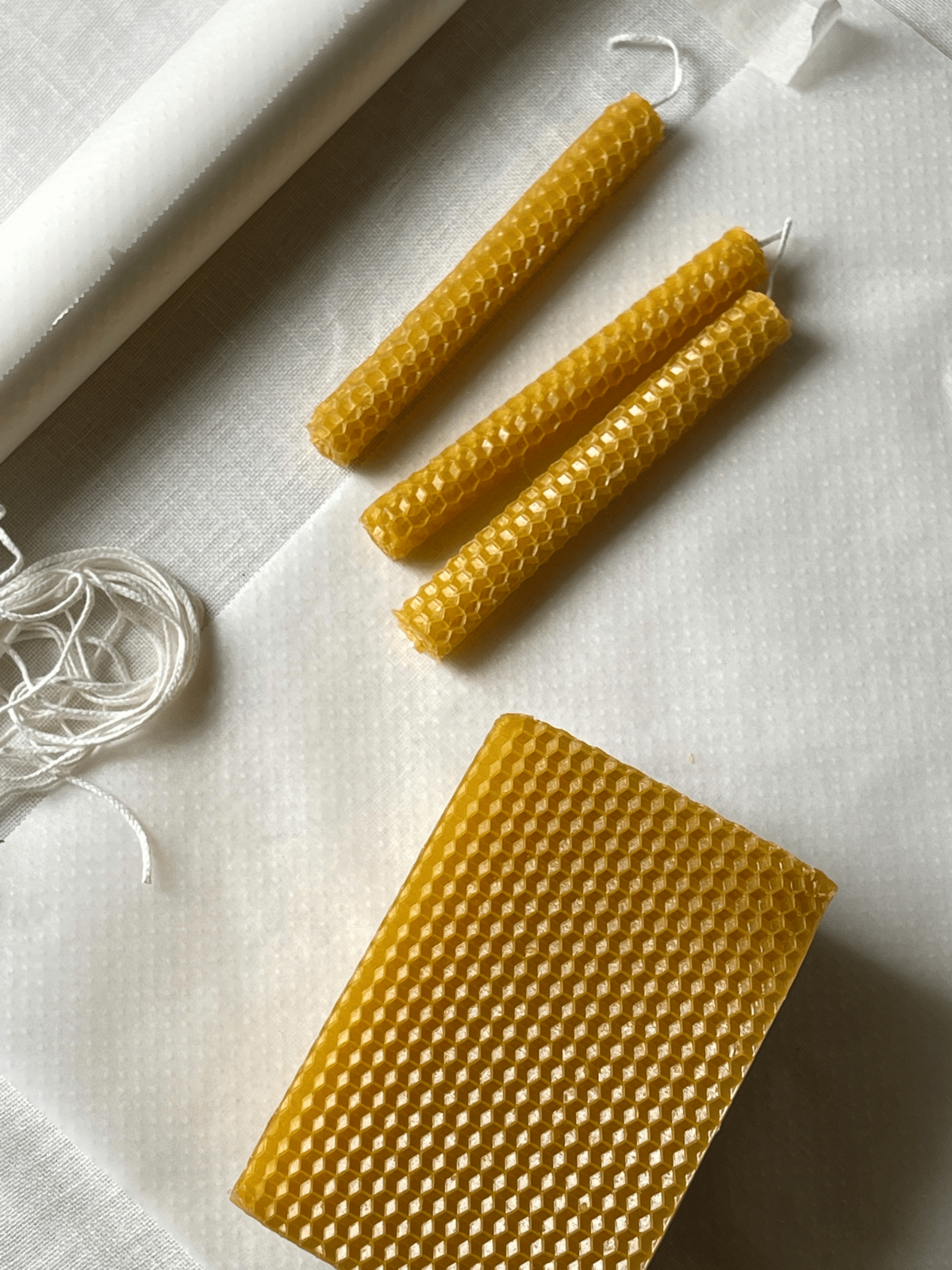 Flat lay of beeswax sheets, cotton wicks, and hand-rolled taper candles for natural eco crafts.