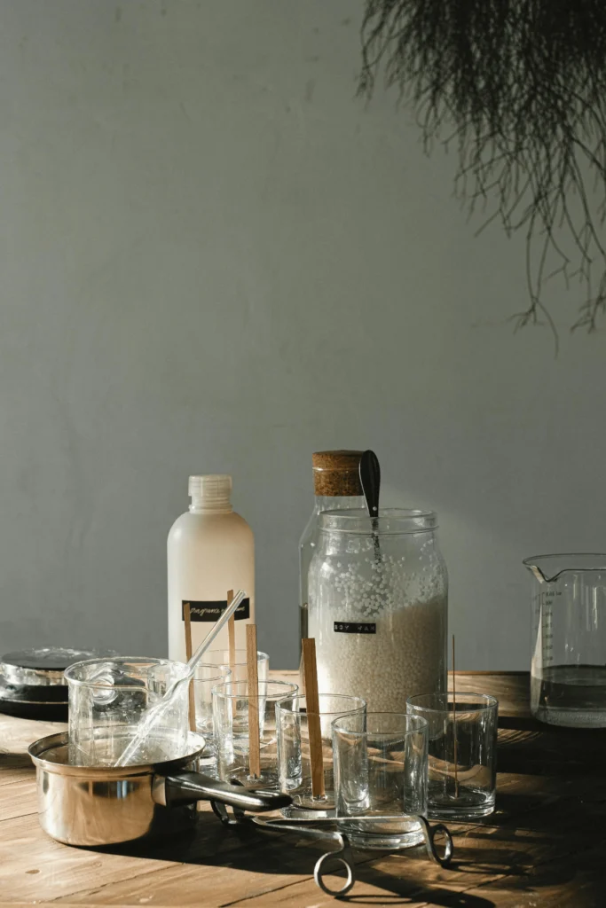 Rustic worktable with soy wax pellets, glass jars with wooden wicks, and tools for DIY candle making