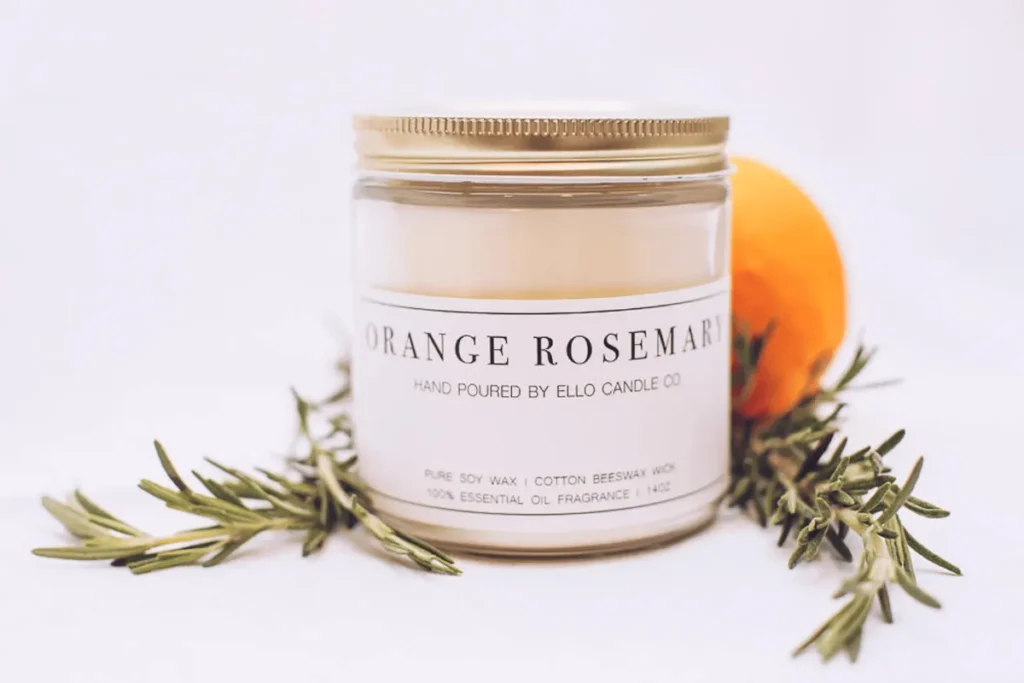 Ello Candle Co. Orange Rosemary soy-beeswax candle in clear jar with gold lid, styled with rosemary sprigs and whole orange