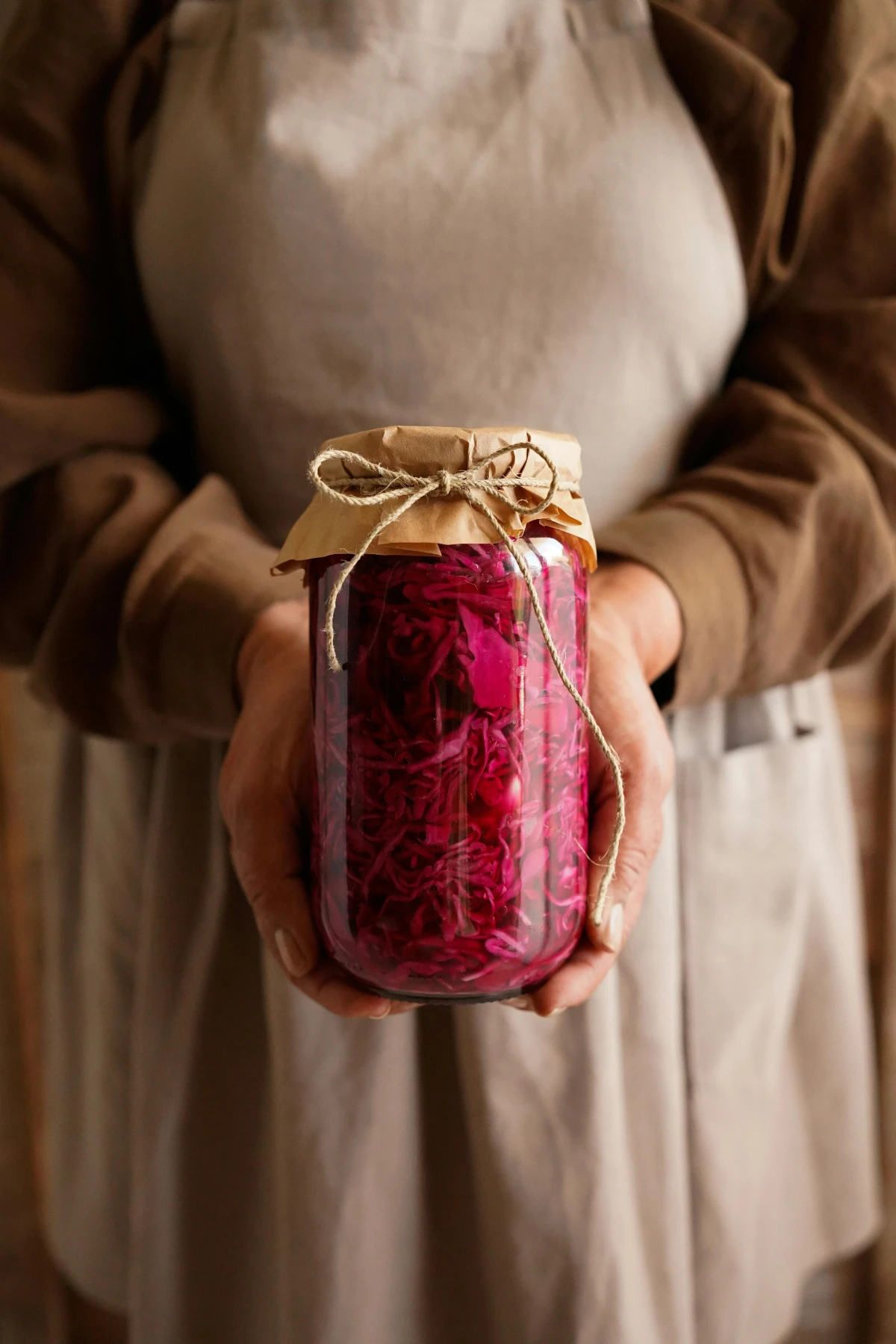 Person holding a glass jar of fermented red cabbage with paper cover and twine, highlighting homemade fermentation.