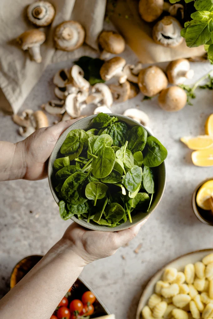 Hands holding fresh spinach with mushrooms and ingredients prepared on a kitchen surface