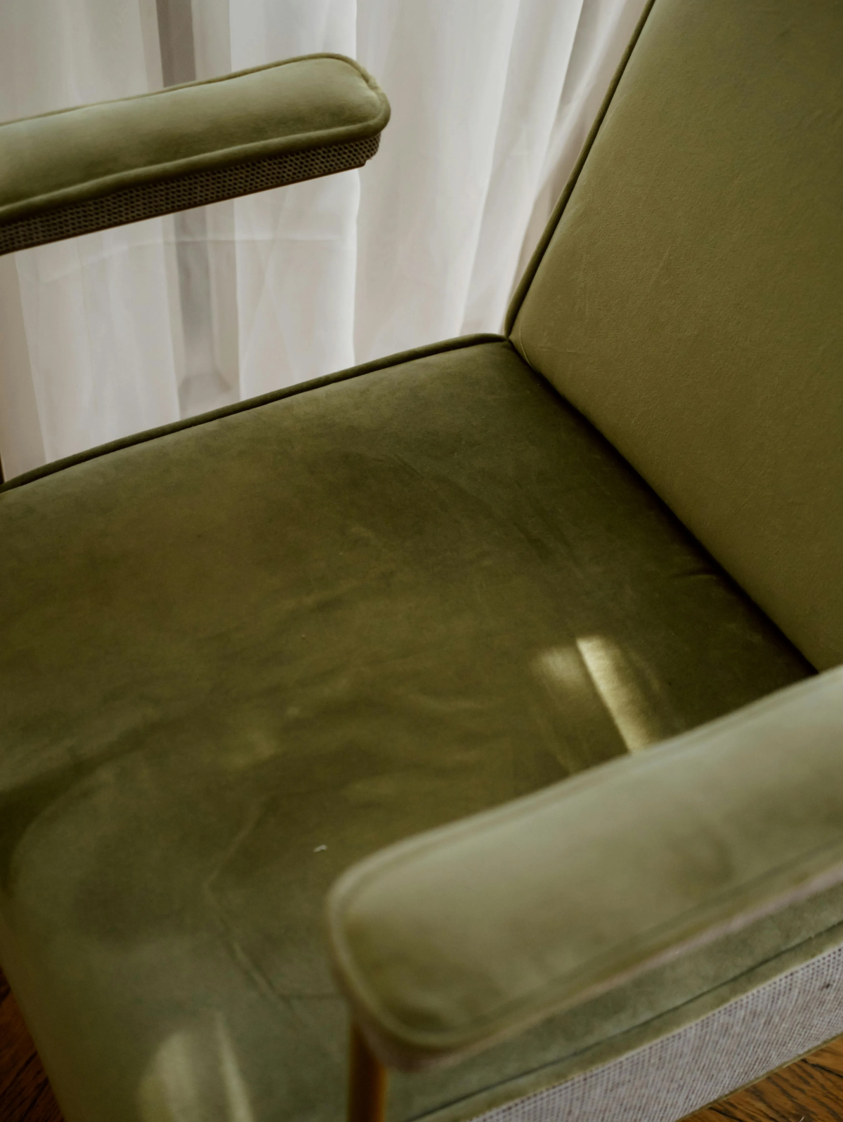 Close-up of modern green velvet accent chair with slim gold legs and armrests, ideal for contemporary living room decor.