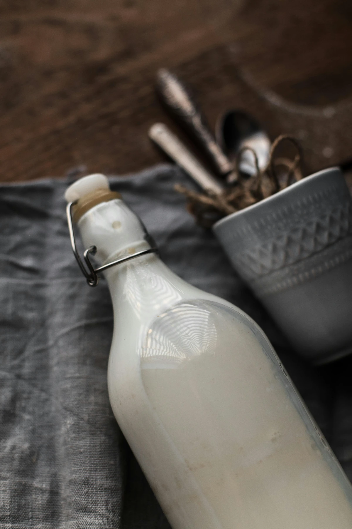 Bottle of homemade plant-based milk on cloth with utensils, soft natural light and minimal kitchen styling.