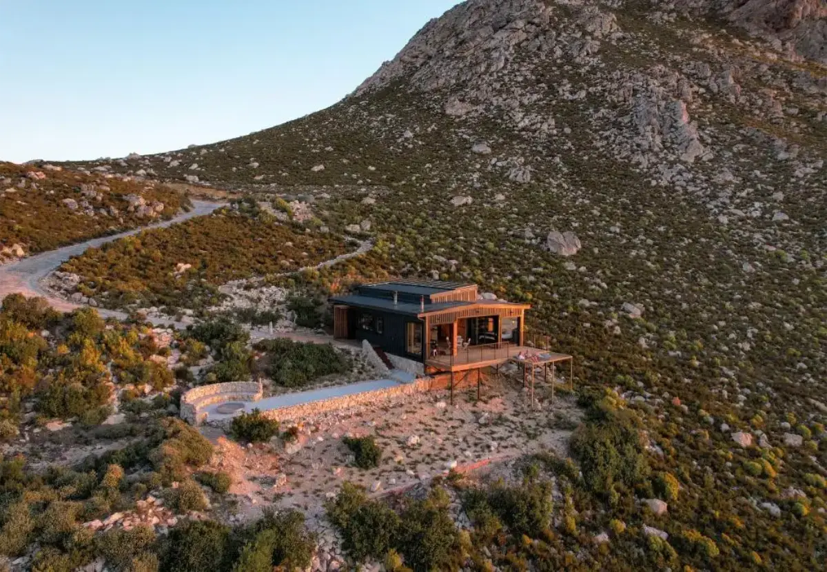 Sunrise aerial of Klein Hangklip off-grid cabin nestled against a rocky Overberg mountainside with sweeping sea-to-summit views.