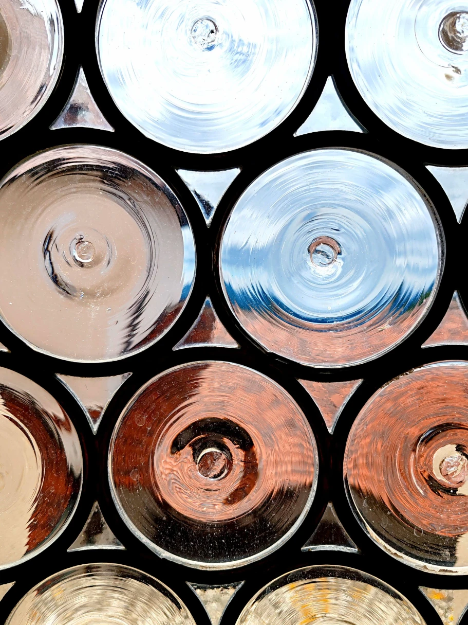 Hand-blown bullseye glass roundels set in dark lead came, a traditional leaded window catching the sky.
