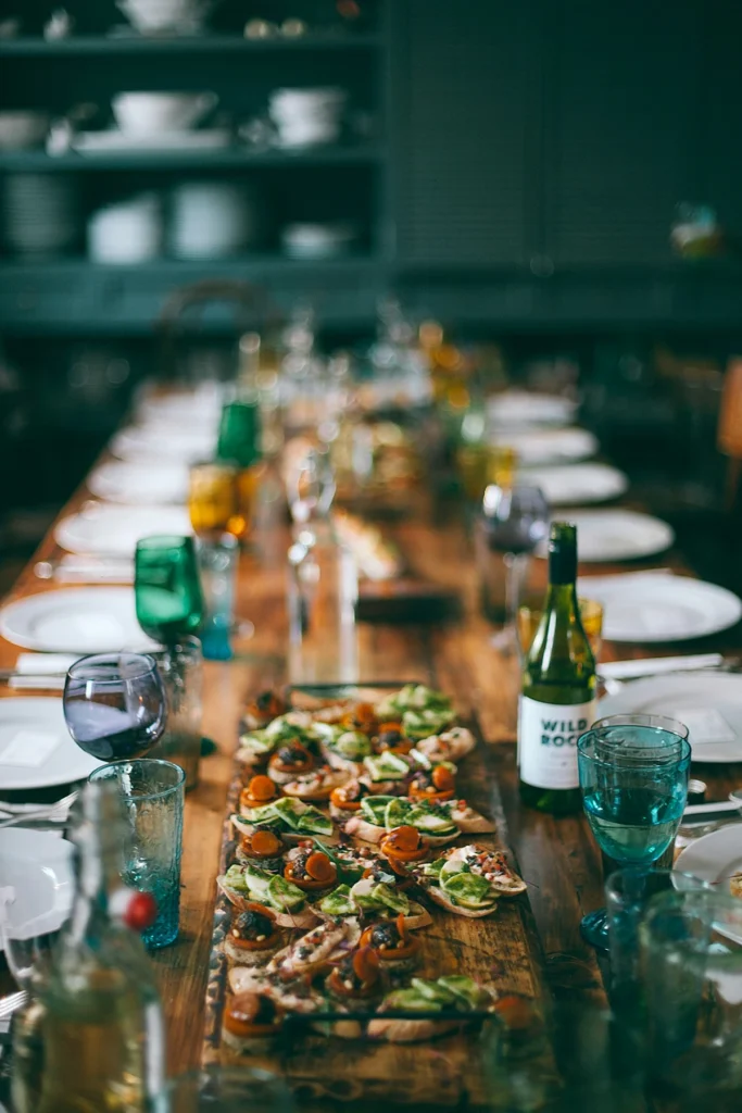 Long wooden table set for dining with seasonal dishes, wine glasses, and shared plates