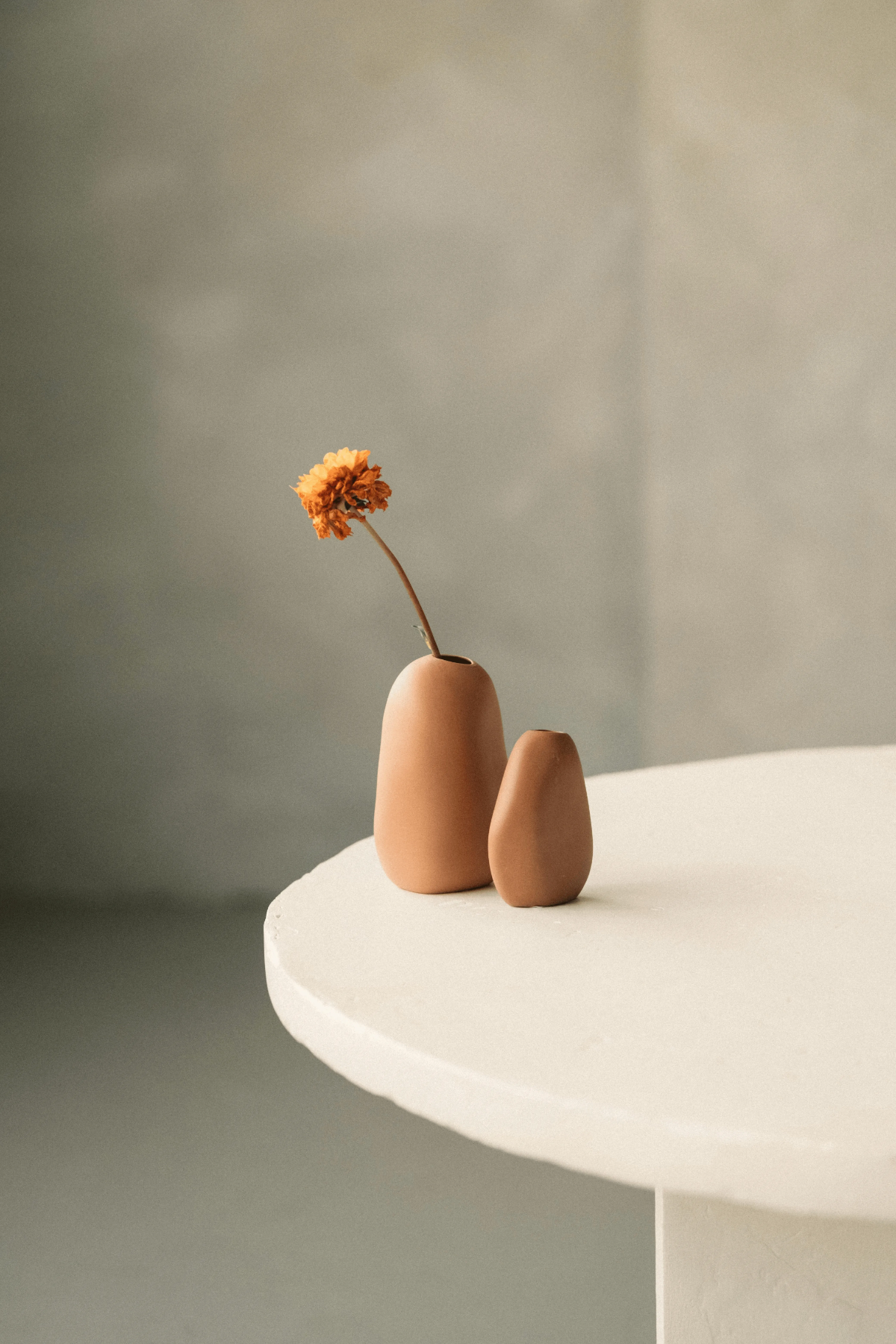 Pair of matte terracotta vases on cream pedestal table.