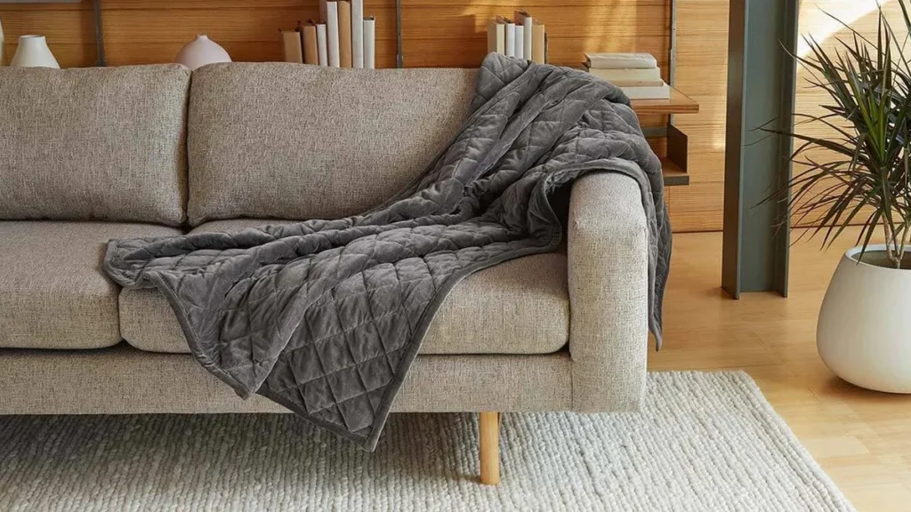 Saatva grey weighted blanket draped over a neutral sofa in a warm, modern living room