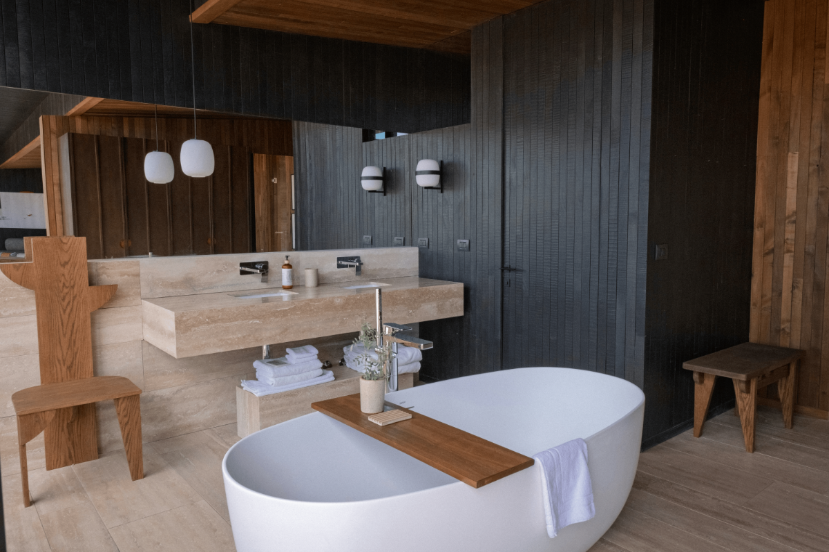 Luxury spa-style bathroom with freestanding oval tub, travertine double vanity and warm wood accents in a modern neutral interior.