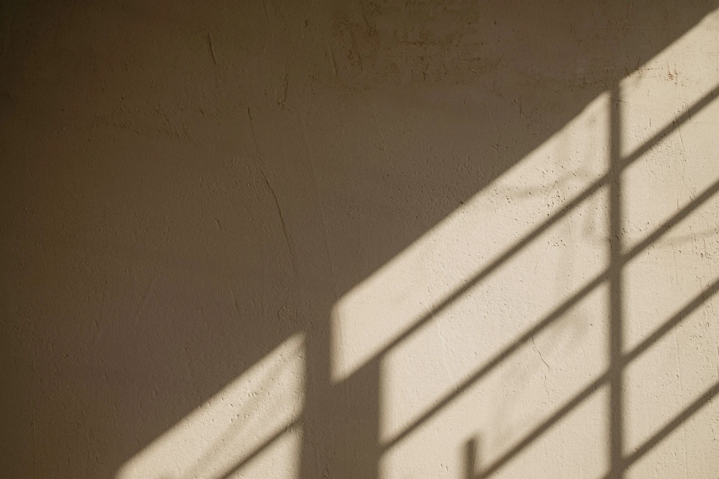 Sunlight casts a window-frame shadow across a textured plaster wall.