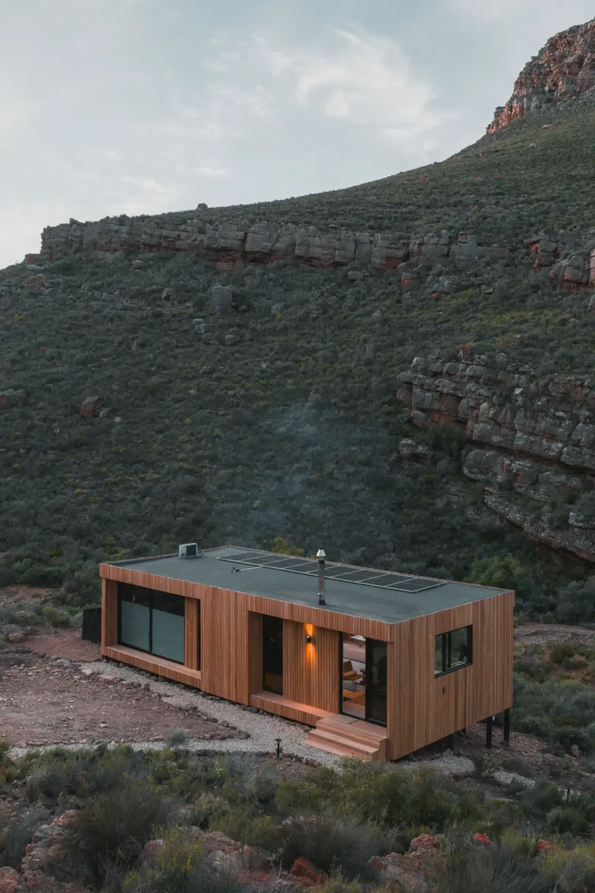 Night view of Verloren retreat, Breede River, bifold glass walls reveal warm-lit kitchen-dining and bedroom suite.