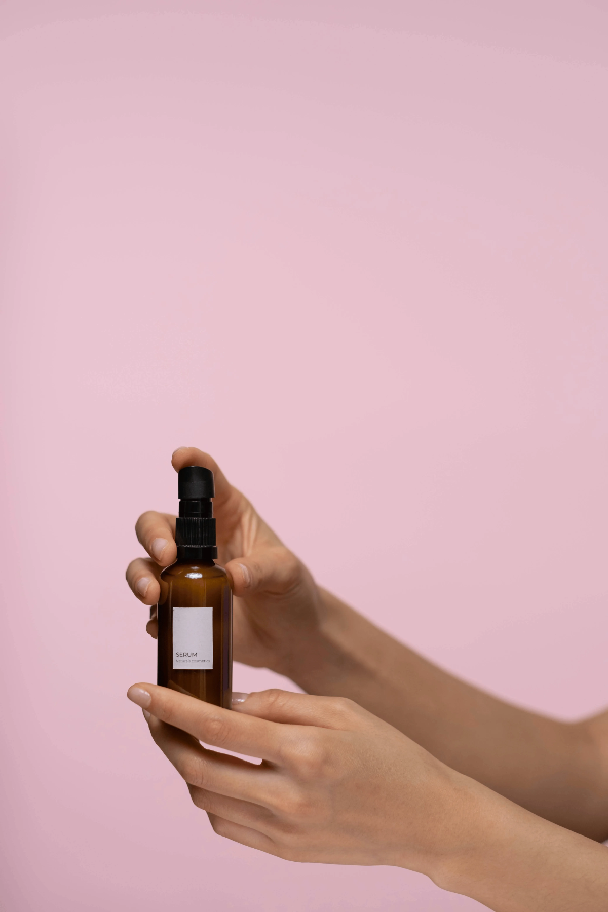 Hands displaying a brown glass pump bottle labeled “Serum".