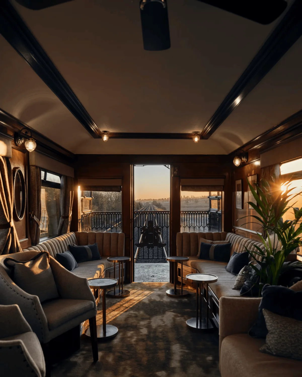 Plush sofas and low tables line the Royal Scotsman’s observation car, glowing in sunset light with an open-air viewing deck ahead.