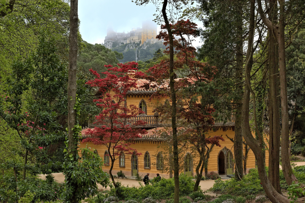 Romantic Swiss-style Chalet da Condessa d’Edla framed by red maples, with misty Pena Palace rising above Sintra Park.