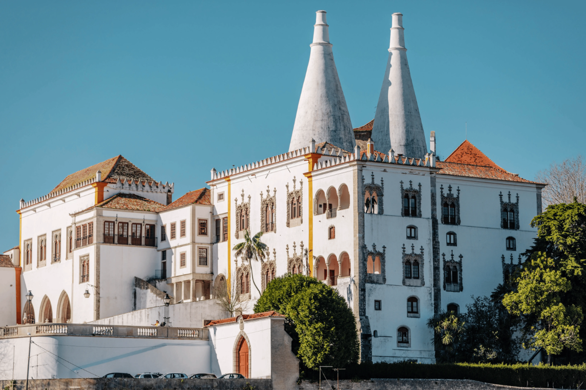 Iconic white National Palace of Sintra with twin conical chimneys and Manueline windows against a clear blue sky.