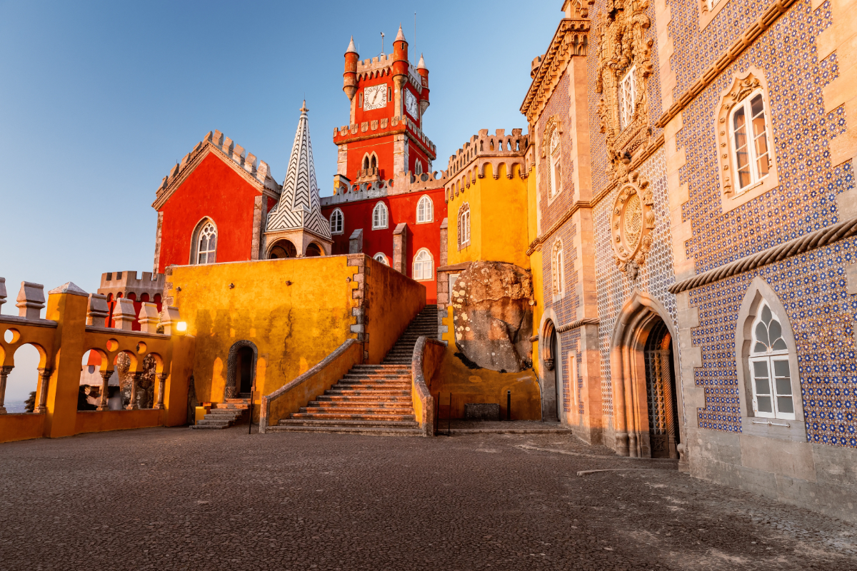 Sunrise light on Pena Palace’s vivid red-and-yellow courtyard, clock tower and tiled façade high above Sintra, Portugal.
