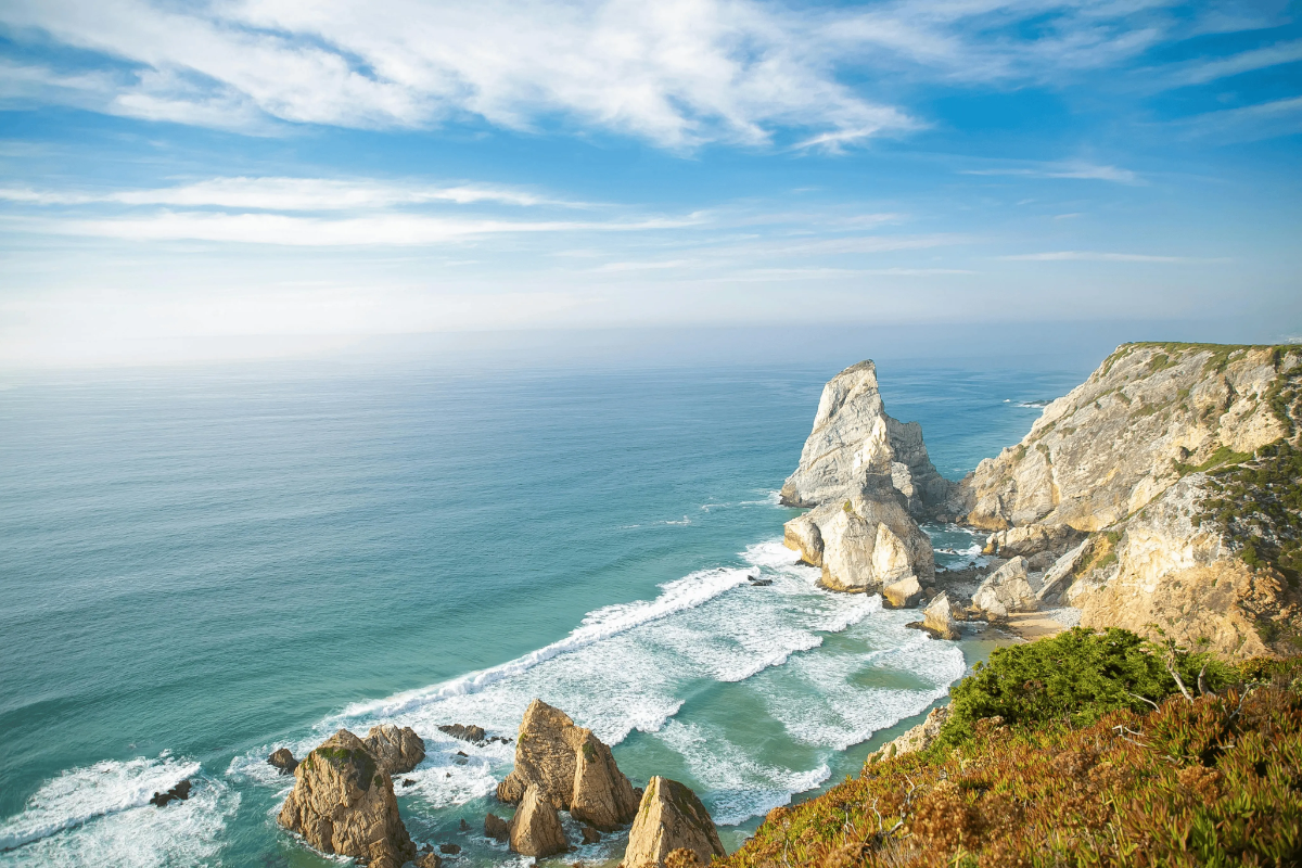 Sweeping view of Praia da Ursa’s jagged sea stack, turquoise Atlantic swells and rugged limestone headland near Sintra.