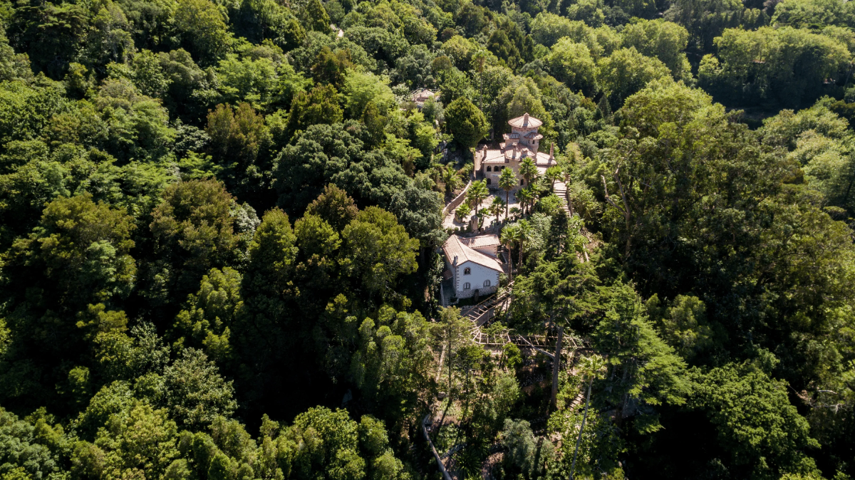 Drone view of Vila Sassetti’s terracotta towers nestled in the lush mountainous forest of Sintra.