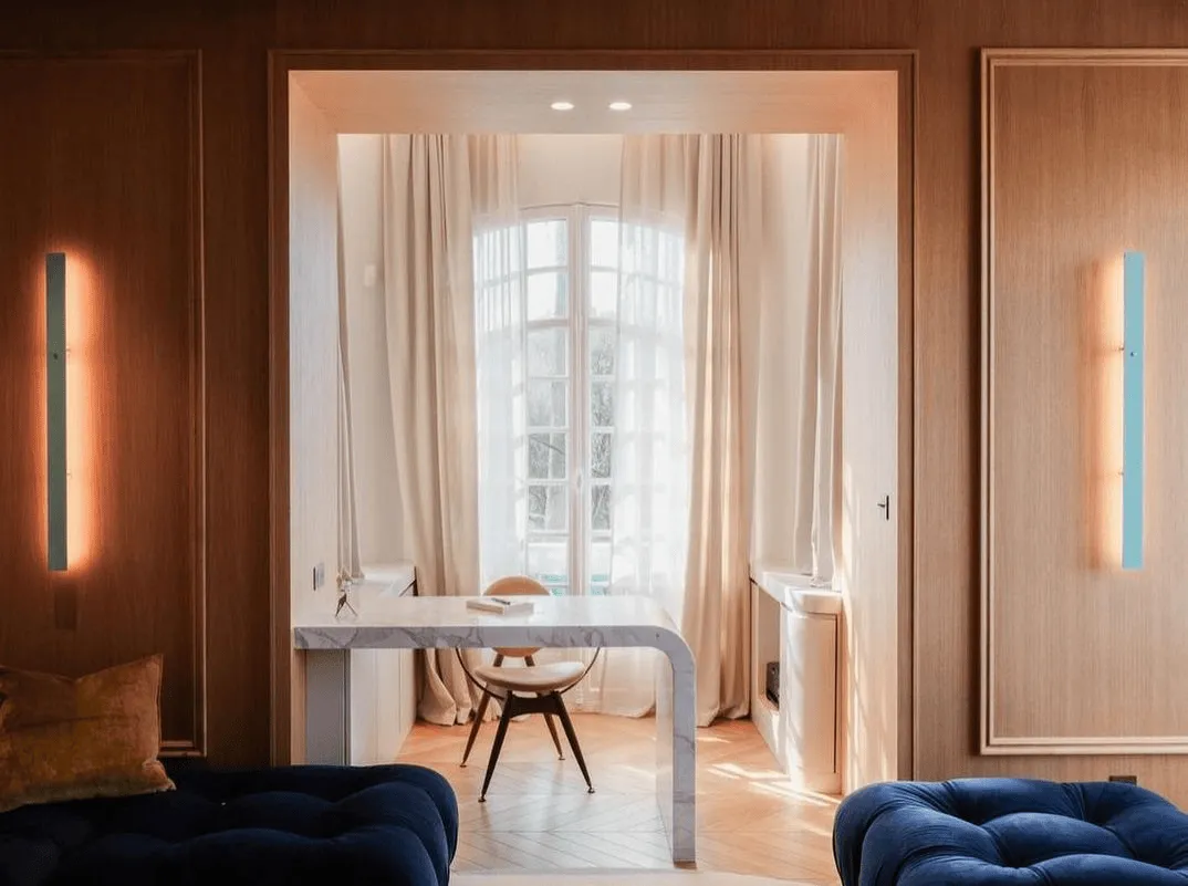Villa Amour by Maison Maju with marble waterfall desk, draped window, light wood paneling, and glowing wall sconces.