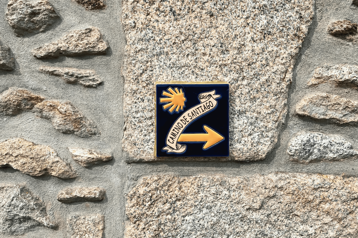 Ceramic way-marker with yellow scallop shell and arrow directing pilgrims along Spain’s Camino de Santiago.